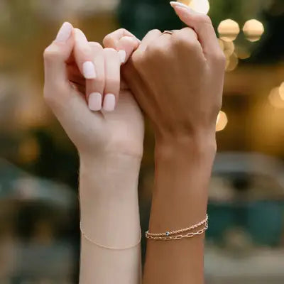 two women wearing permanent jewelry with pinkies locked together