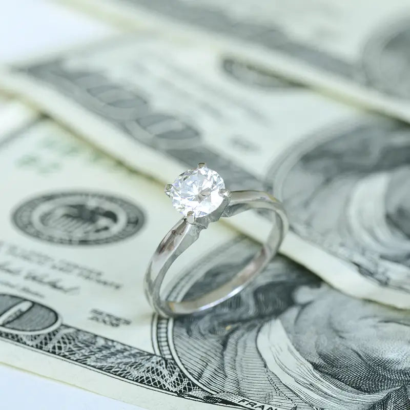 a diamond ring and cash on white desk