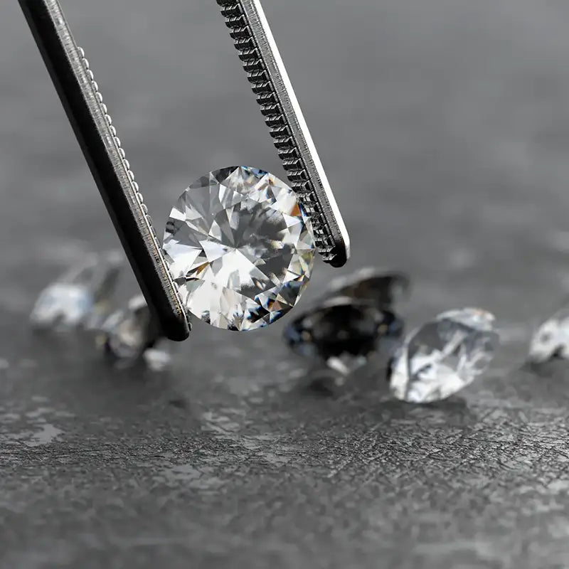 a loose diamond held with pliers, more loose diamonds in background