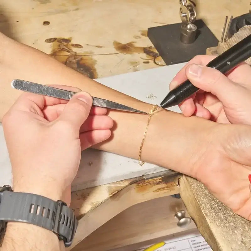 permanent jewelry being attached to customer's arm, wooden surface in background